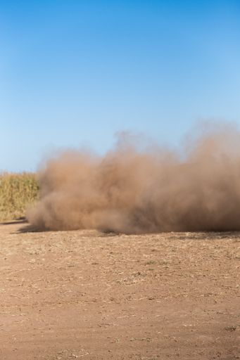 A vertical shot of a rally car raising dust while racing on a desert