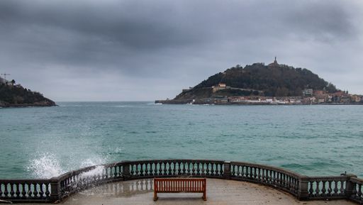 A high angle shot of a bench at the sea near a port in San Sebastian, Spain