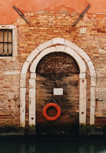 A vertical shot of a red brick wall with a hanging lifeboat in Venice, Italy