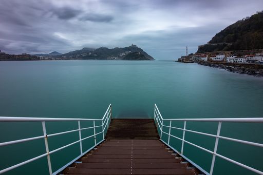 A boardwalk with metal railings at the sea under dark storm clouds in San Sebastian, Spain