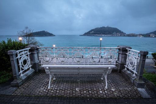 A high angle shot of a bench at the sea near a port in San Sebastian, Spain