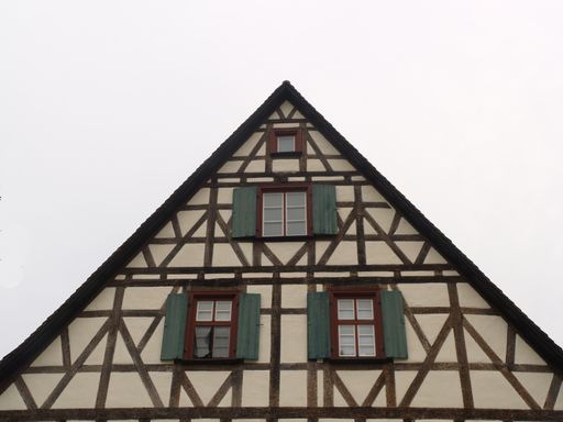 A low angle shot of a half-timbered A-frame house roofing with windows against a white sky
