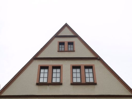 A low angle shot of an A-frame house roofing with windows against a white sky