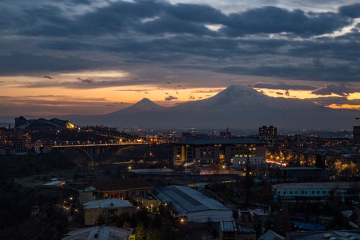 A scenic view of Yerevan, Armenia illuminated by city lights on a background of Mount Ararat at sunset