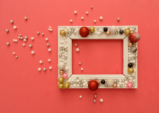 A top view of New Year decorations and balls arranged around a rectangular frame on a pink background