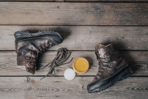 Outdoor boots with wax. Waxing and cleaning outdoor leather shoes. Maintanance of footwear, wooden background.