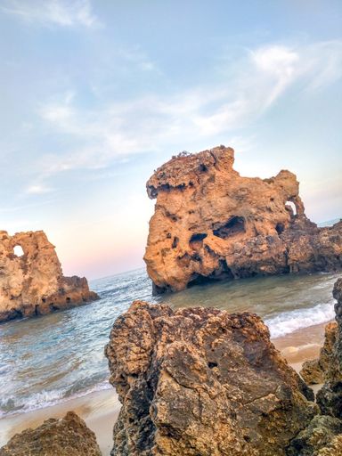 A vertical shot of a seashore with huge cliffs under the blue sky