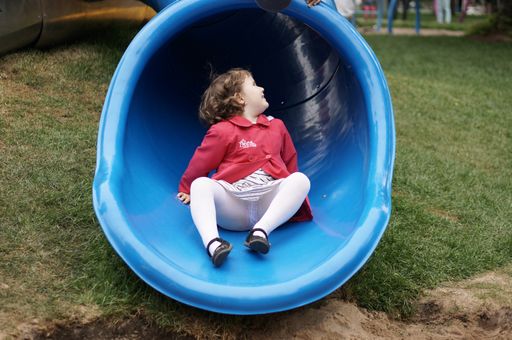 A closeup of a small child sliding down a blue slide at a playground in Poland