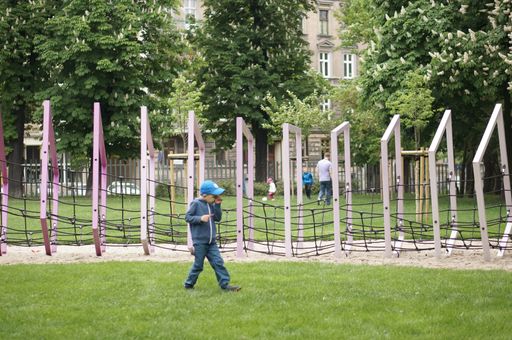 A young boy walking on green grass in a playground in Poland