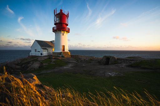 Historic red white lighthouse on the edge of rocky sea coast, South Norway, Lindesnes Fyr beacon. At Sunset
