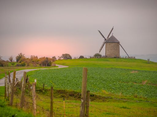 A beautiful shot of large green meadows with a windmill on the background