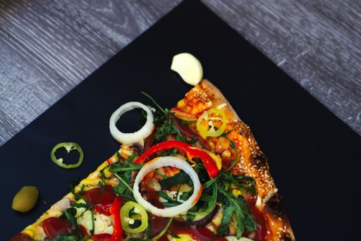 A high angle shot of a delicious slice of pizza with different ingredients on a black surface - Perfect background for Pizzerias
