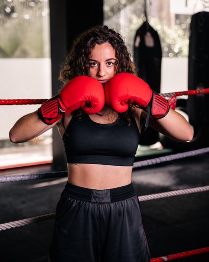A vertical shot of a curly Caucasian female posing with red boxing gloves in the ring