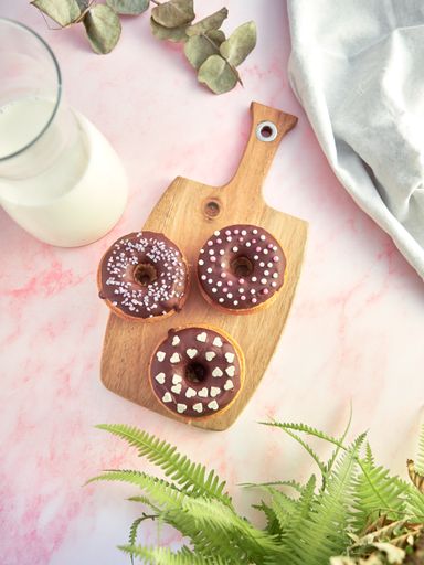 A top view of chocolate donuts on a wooden tray on a light pink table