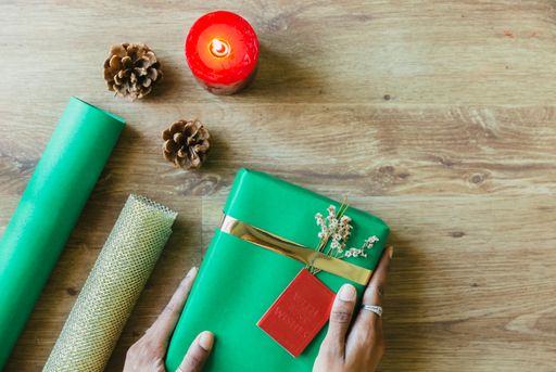 A top view of hands holding a wrapped gift over a wooden table with wrapping items - concept for the holiday season
