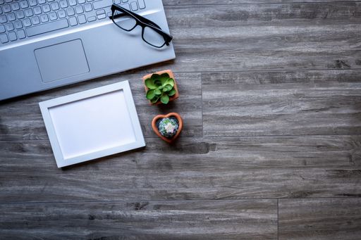 A closeup of a laptop and glasses on a wooden surface