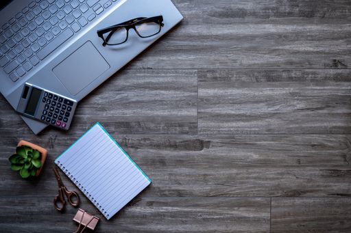 A closeup of a laptop and glasses on a wooden surface