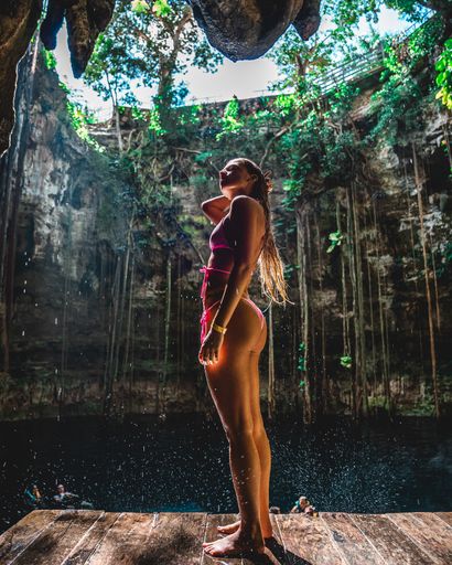A vertical shot of a young sexy caucasian female in a pink bikini standing under a waterfall