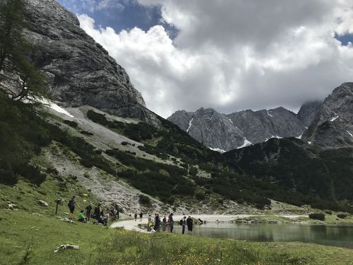 A breathtaking shot of a nature with a lake and tourists near it under a cloudy sky