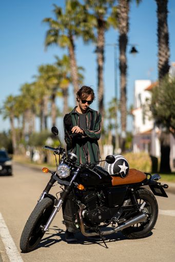 A closeup of a man with a motorcycle posing in stylish clothes