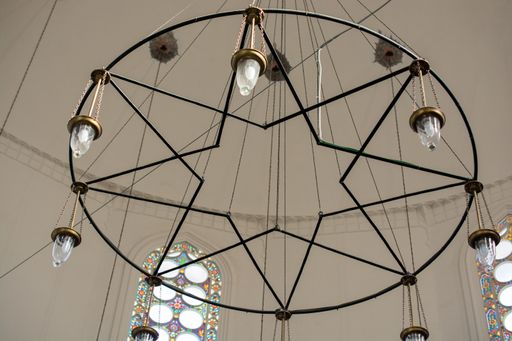 A low angle shot of a chandelier designed like a star in a white room with a colorful window