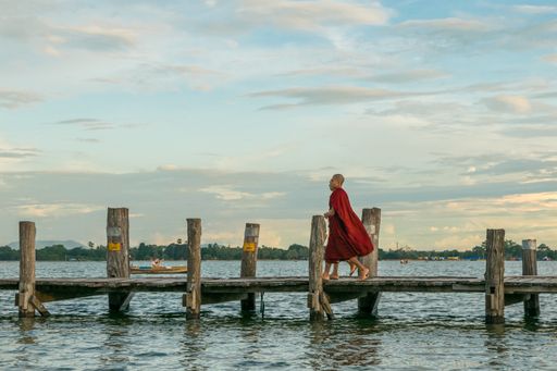 Buddhist monks walking on U-Bein bridge, during sunset, in Taungthaman Lake near Amarapura, close to the city of Mandalay in Myanmar, Burma, SE Asia