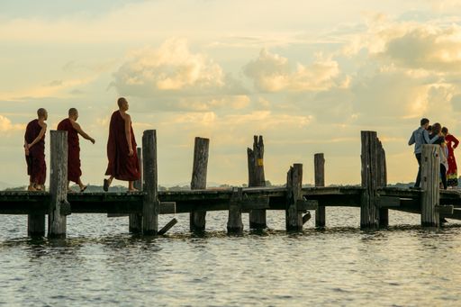 Buddhist monks walking on U-Bein bridge, during sunset, in Taungthaman Lake near Amarapura, close to the city of Mandalay in Myanmar, Burma, SE Asia