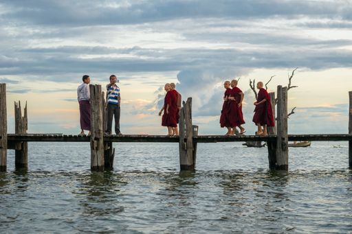 Buddhist monks walking on U-Bein bridge, during sunset, in Taungthaman Lake near Amarapura, close to the city of Mandalay in Myanmar, Burma, SE Asia