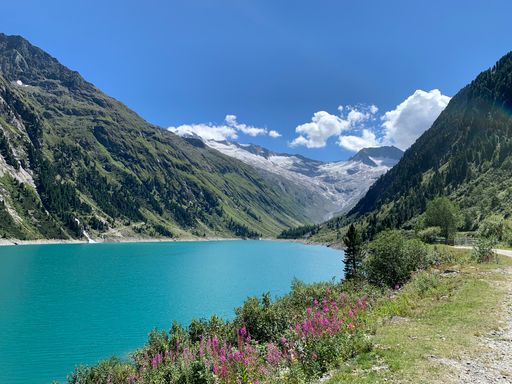 A landscape view of the Schlegeis Basin surrounded by mountains under a blue cloudy sky on a sunny day