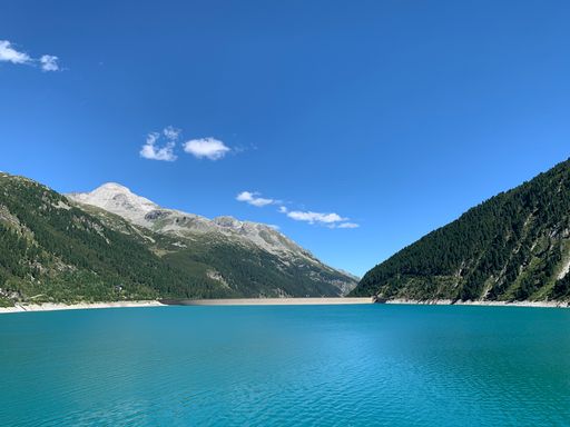 A landscape view of the Schlegeis Basin surrounded by mountains under a blue cloudy sky on a sunny day