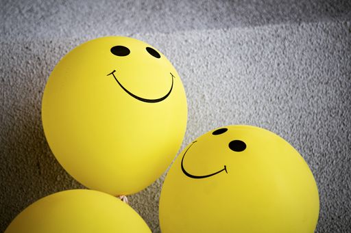 A closeup shot of yellow balloons with smiley faces on them by a concrete wall