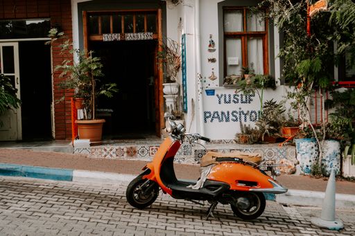 Orange Vespa parked in front of small cozy mediterranean house. Mediterranean house with scooter parking in front of it