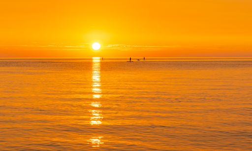 The beautiful view of an orange sunset reflected on the sea with surfers at Lake Michigan