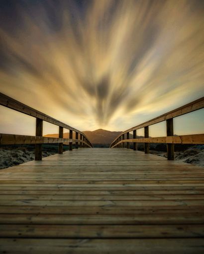 A vertical view of the sunset at the beach and the wooden bridge