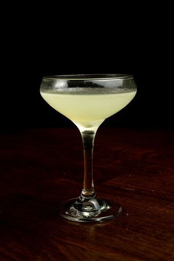 A vertical shot of a glass of Corpse Reviver cocktail on the table with a dark blurry background