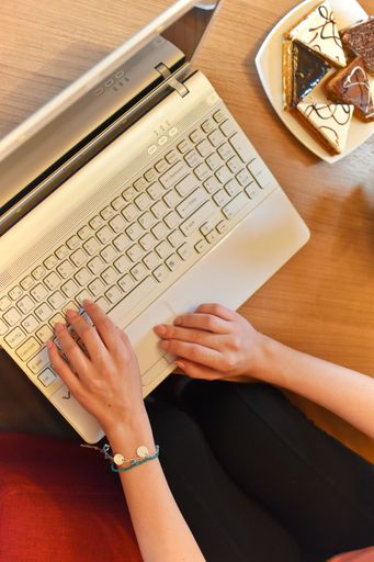 A vertical top view of the female sitting on the red sofa and working on laptop with dessert next to her