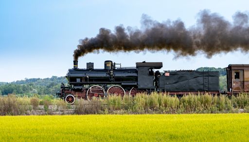 Vintage steam train with ancient locomotive and old carriages runs on the tracks in the countryside