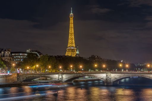 The beautiful illuminated Eiffel Tower at night behind the Pont des Invalides bridge over Seine river