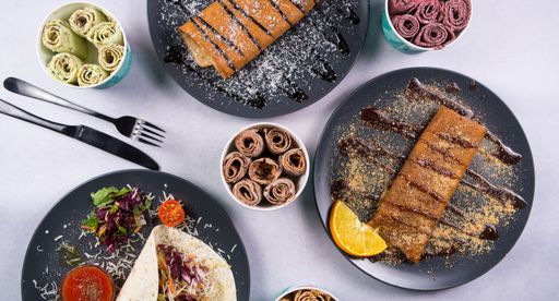 A top view of sweet crepes and tortilla in gray plates and ice cream in different flavors with fork and knife on a white table