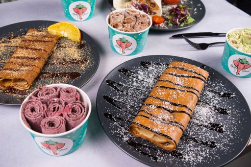 A close-up shot of sweet crepes and tortilla in gray plates and ice cream in different flavors with fork and knife on a white table