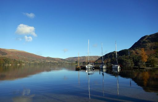 The reflection of yachts on Lake Ullswater under a blue sky on a sunny day