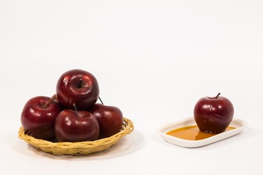 A pile of red apples and a single red apple on a white plate with honey isolated on a white background - Jewish New Year - Rosh Hashanah