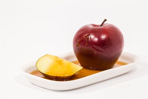 A whole red apple and apple slice with drops of honey on white plate in white background.