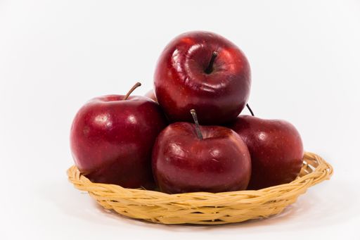 A closeup shot of red apples in wicker basket on white background.