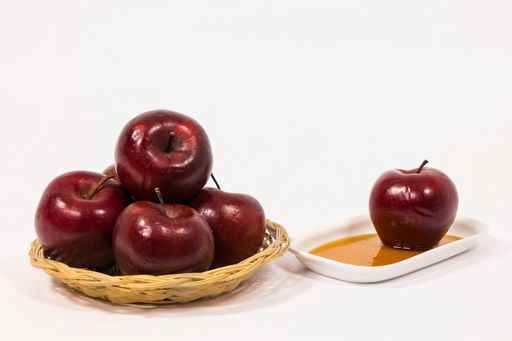 The pile of red apples and red apples on a white plate with honey is isolated on a white background. Symbols of Jewish New Year - Rosh Hashanah.