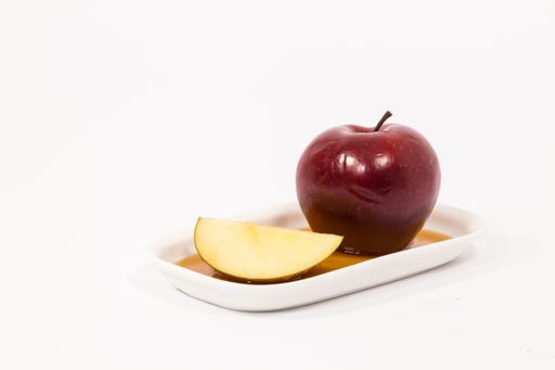 The red apple and red apple slice on white plate with honey isolated on a white background. Symbols of Jewish New Year - Rosh Hashanah.