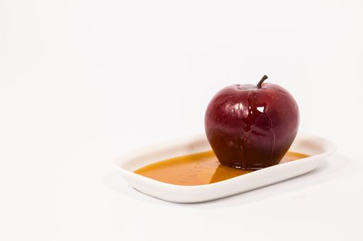 The red apple with drops of honey on a white plate with honey isolated on a white background. Symbols of Jewish New Year - Rosh Hashanah.