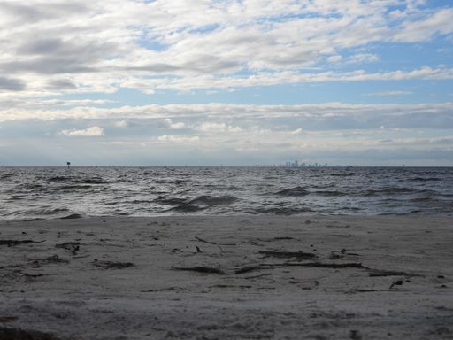A mesmerizing cloudscape over the wavy sea water and the wet sandy coast with a city in the background