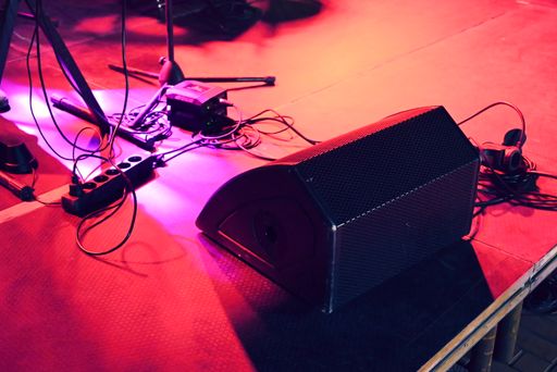 A concert stage under a red light with a lot of wires, mic stands and a big speaker on the floor