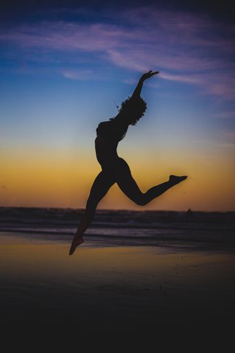 A vertical photo of a silhouette of a young woman dancing in the air